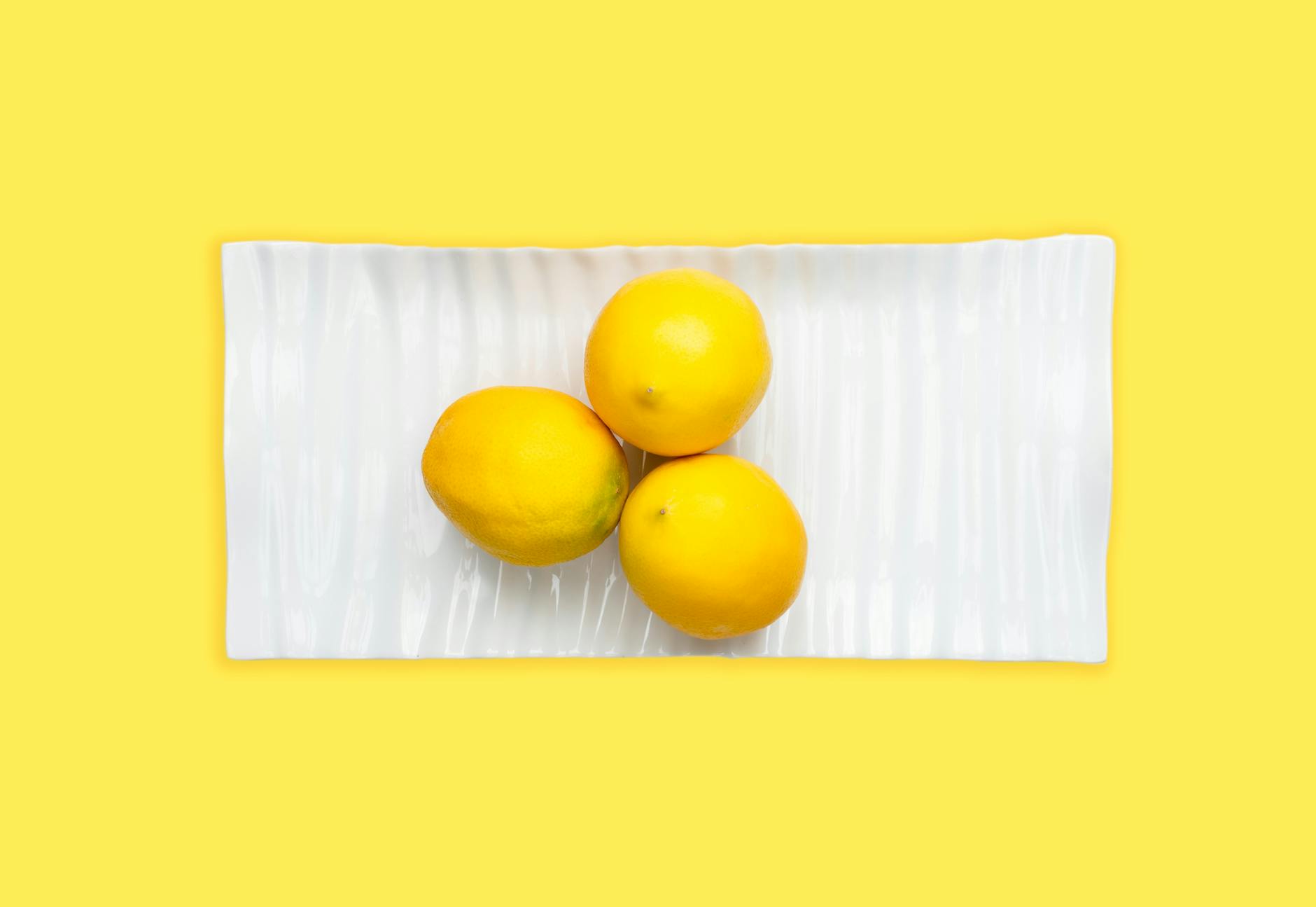 A blue lemon suction vibrator surrounded by fresh citrus and flowers on a bright yellow background