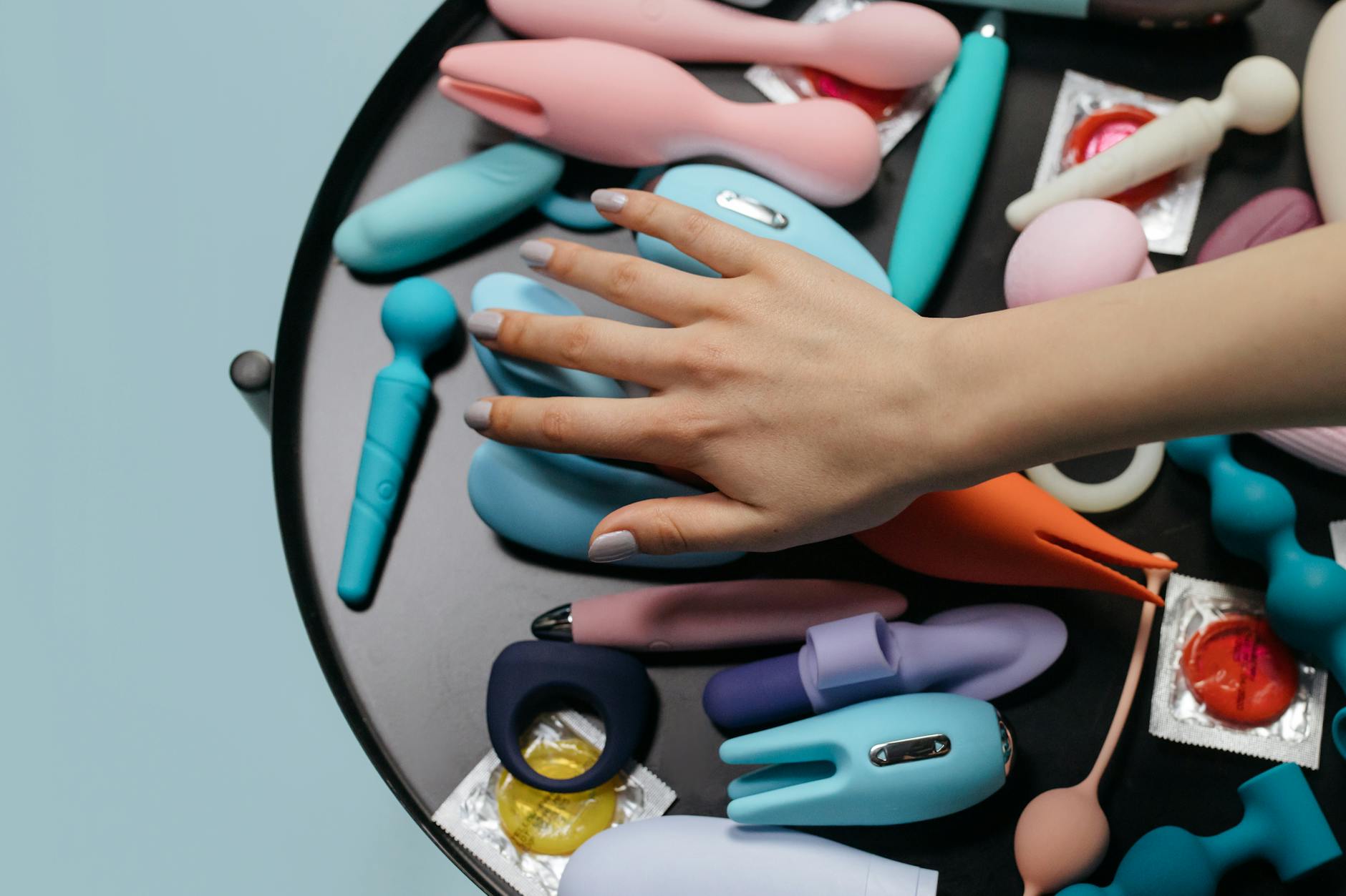 Primer plano de una mujer sosteniendo un vibrador rosa, con libros de arte de fondo, enfatizando temas íntimos y personales.