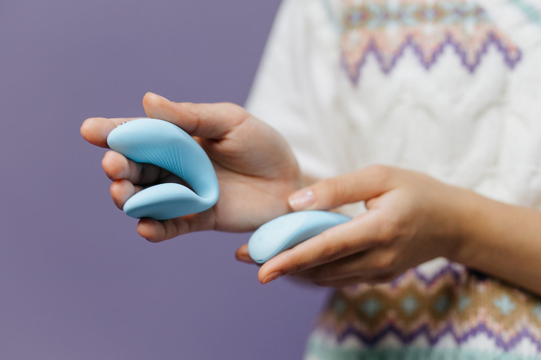 Manos sosteniendo un vibrador azul elegante contra un fondo morado suave