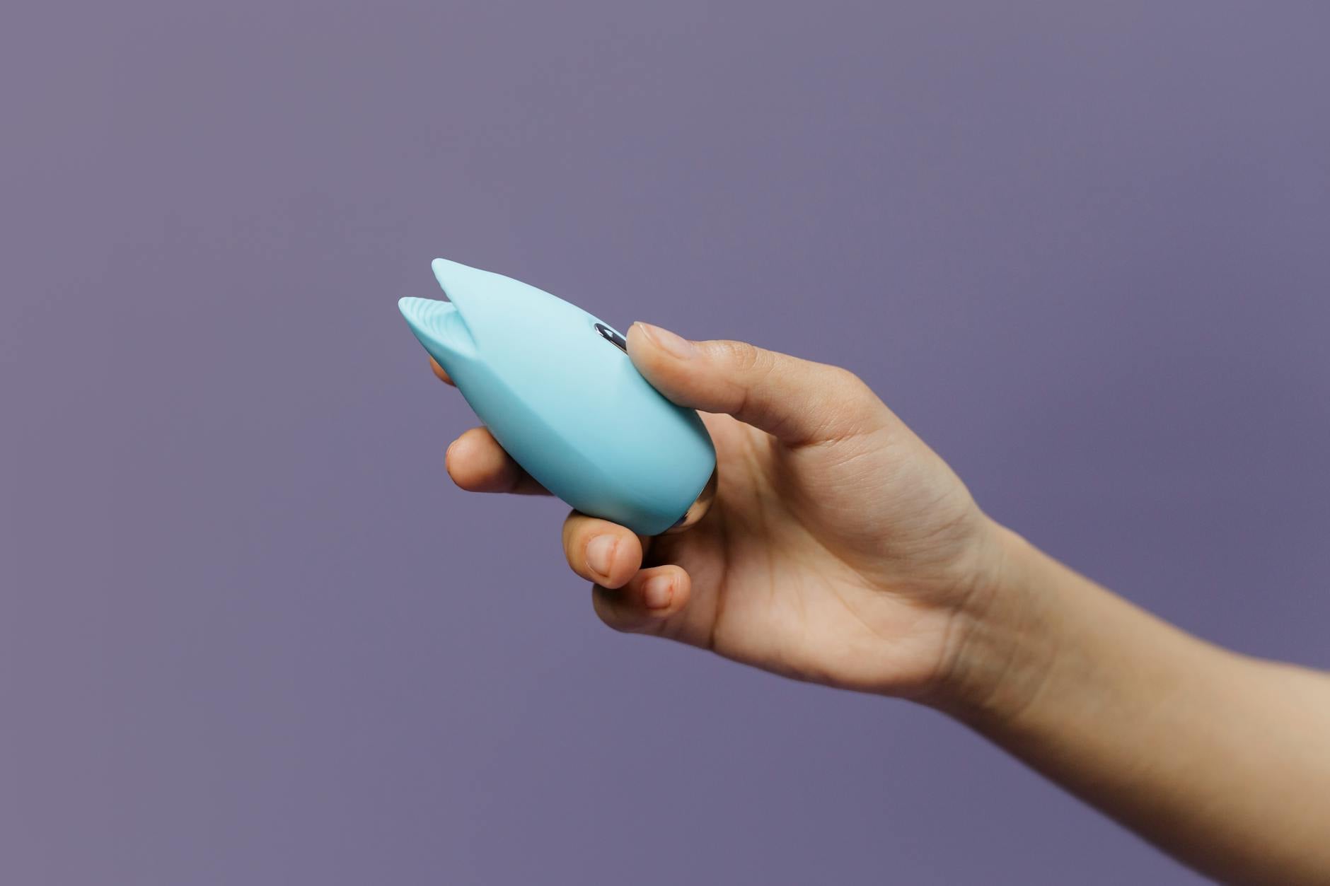 Un vibrador de silicona azul sostenido en la mano contra un fondo morado sólido, promoviendo el amor propio y la sexualidad.
