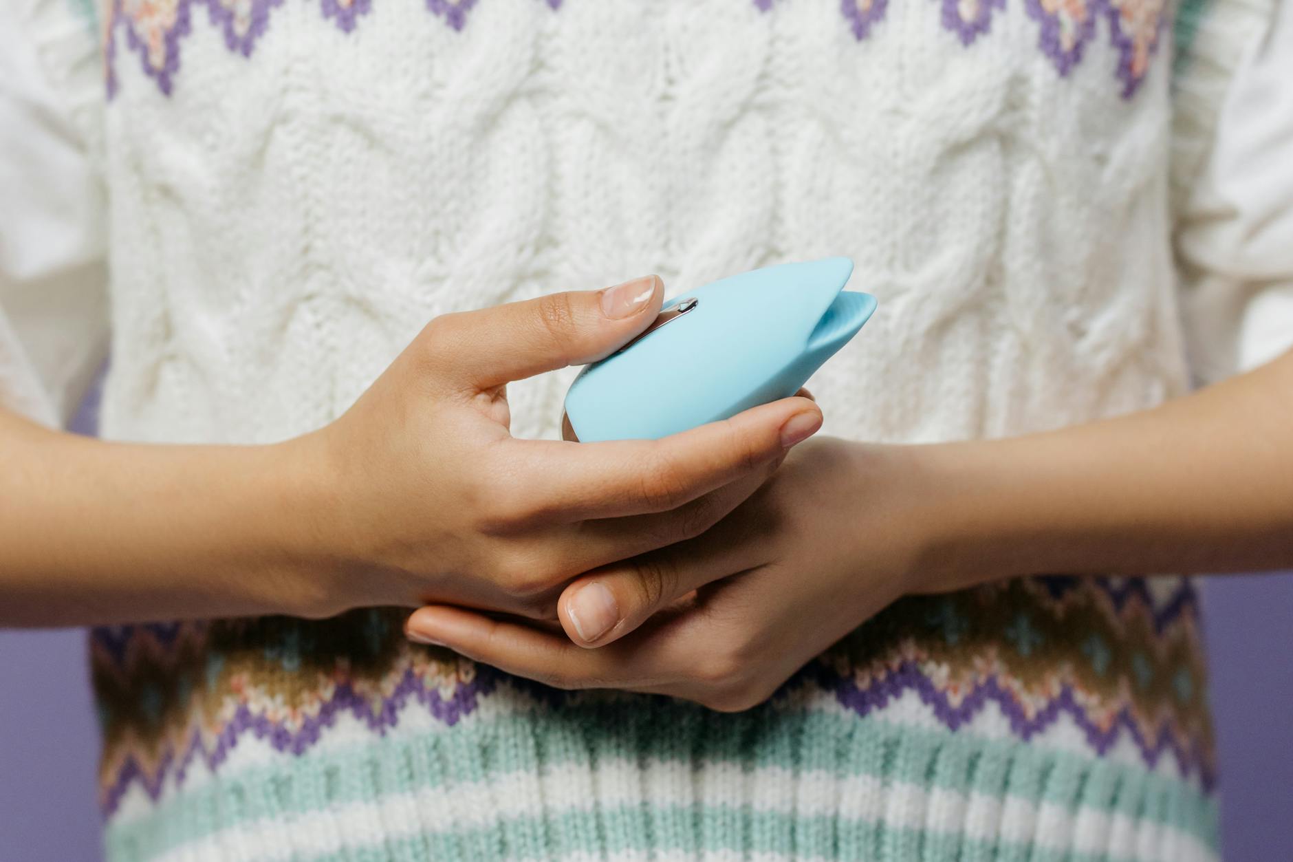 Manos sosteniendo un vibrador azul personal contra un suéter tejido.