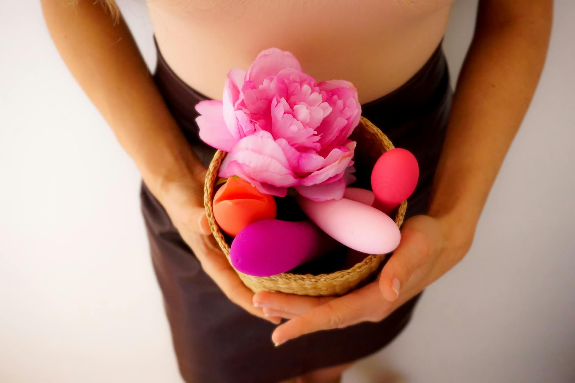 Hands holding colorful vibrators and toys in a basket